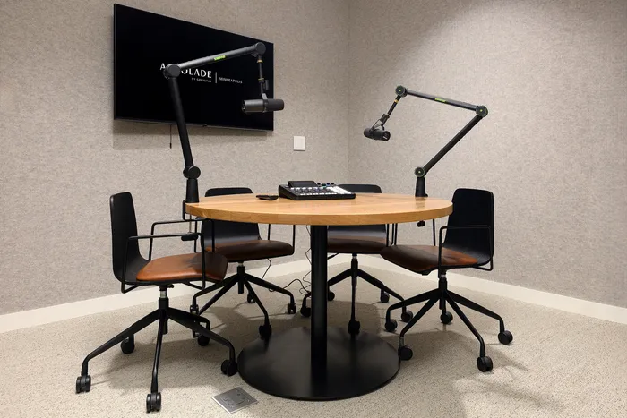 Modern, professional podcast studio with a round wooden table, three ergonomic chairs, high-quality microphones, and a sleek control panel for seamless recording.