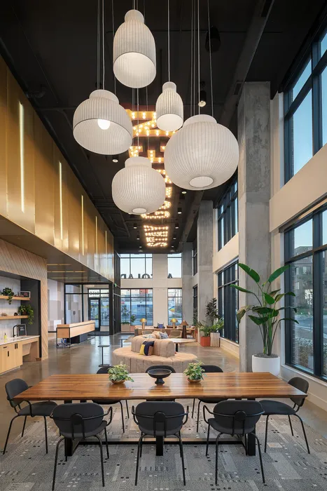Modern, spacious lounge area with chic pendant lighting, natural wood table, and comfortable seating, surrounded by large windows and lush greenery.