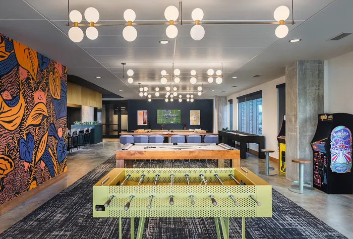 Modern entertainment lounge with vibrant wall art, stylish lighting, and game options including foosball and arcade machines.