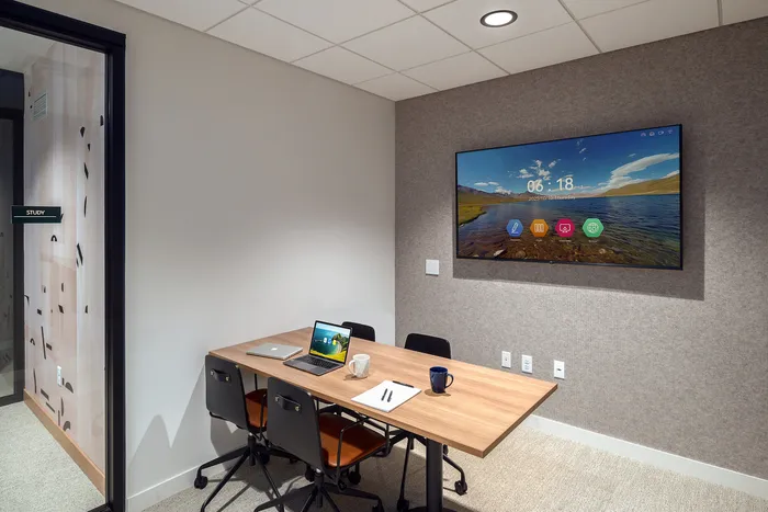 Modern study room showcasing a sleek wooden desk with chairs, a wall-mounted screen, and minimalist decor.