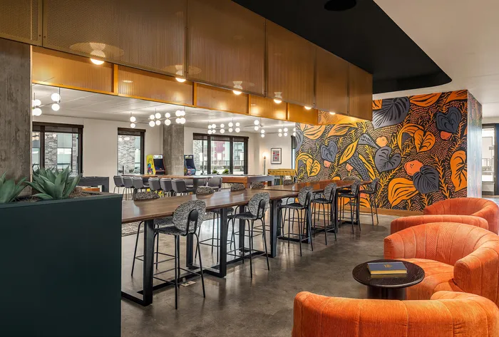 Chic communal lounge with vibrant orange seating, artistic wall mural, and modern lighting, perfect for relaxation and social gatherings.
