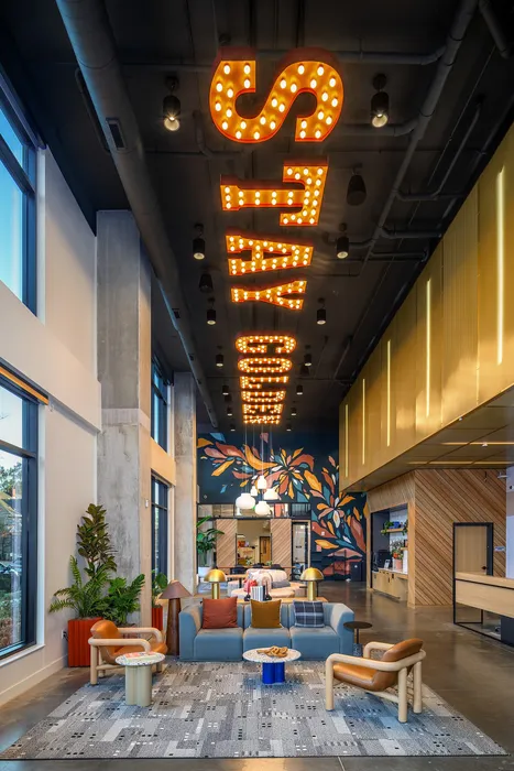 Chic and modern lobby featuring vibrant lighting saying 'STAY COZY', artistic murals, and stylish seating area with colorful decor.