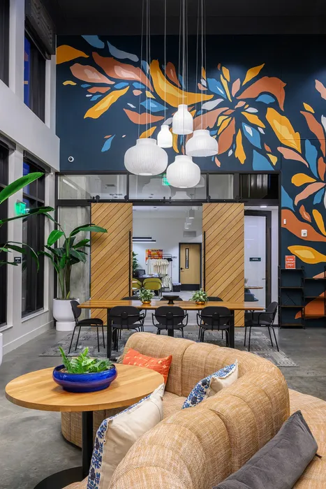 Modern lounge area with a vibrant mural, elegant pendant lighting, stylish seating, and lush greenery, creating a welcoming ambiance.