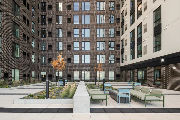 Modern apartment building courtyard with stylish landscaping, contemporary seating, and vibrant autumn trees, offering a serene outdoor retreat.