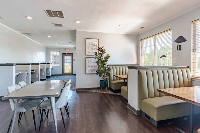 Modern communal space with booths and a meeting table, featuring stylish decor, large windows, and natural light.