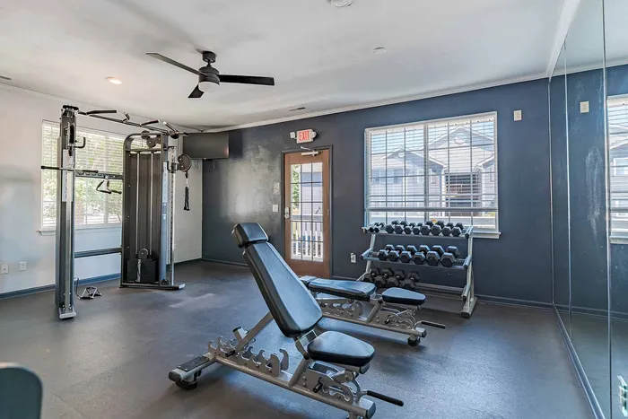 Inviting fitness room featuring modern gym equipment, free weights, and ample natural light from large windows for an energizing workout experience.