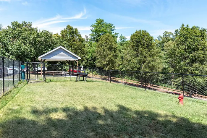 Beautifully landscaped dog park with a pavilion and secure fencing, surrounded by lush greenery and clear blue skies.