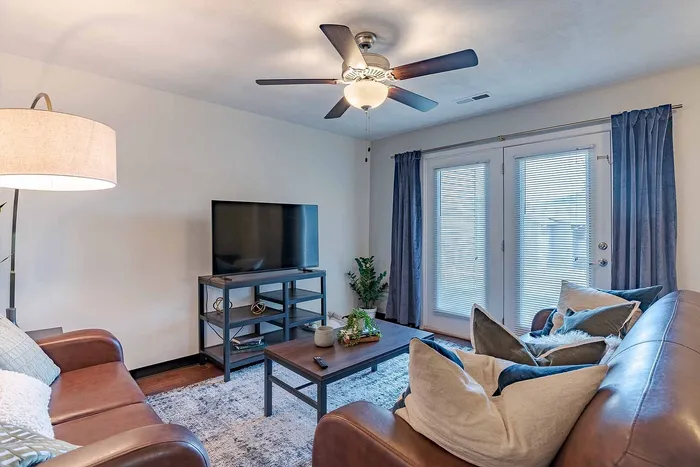Inviting living room with elegant leather sofas, stylish decor, large TV, and natural light through French doors.