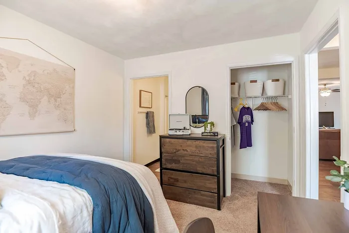 Cozy bedroom with modern decor, featuring a stylish wooden dresser, wall art, and an open closet with ample storage space.