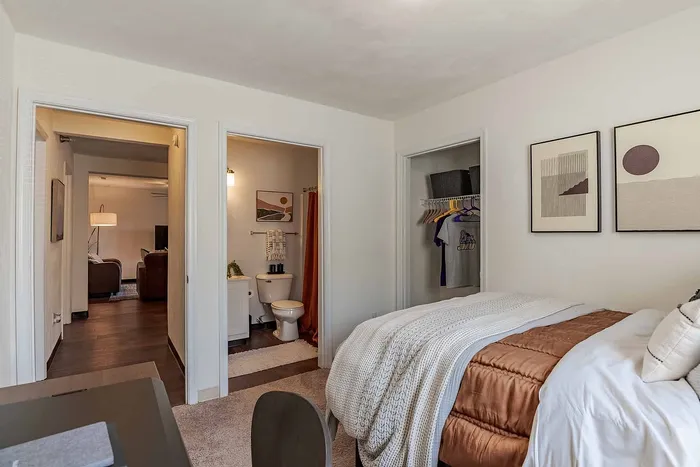 Inviting bedroom with plush bedding, modern artwork, and convenient access to a cozy living area and stylish bathroom, perfect for comfort and relaxation.