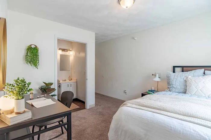 Bright and cozy bedroom with an inviting bed, elegant desk, and a compact en-suite bathroom, perfect for comfort and relaxation.