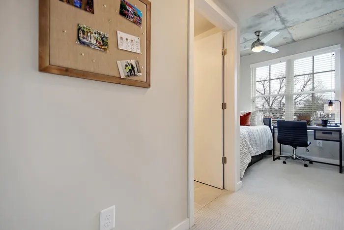 Bright and inviting bedroom with modern ceiling fan, large windows, and cozy desk area, perfect for work-from-home or studying.