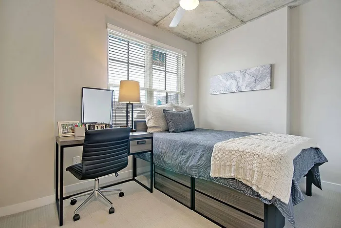Cozy bedroom with a plush bed, stylish desk, and natural light from large windows, offering a serene and inviting atmosphere.