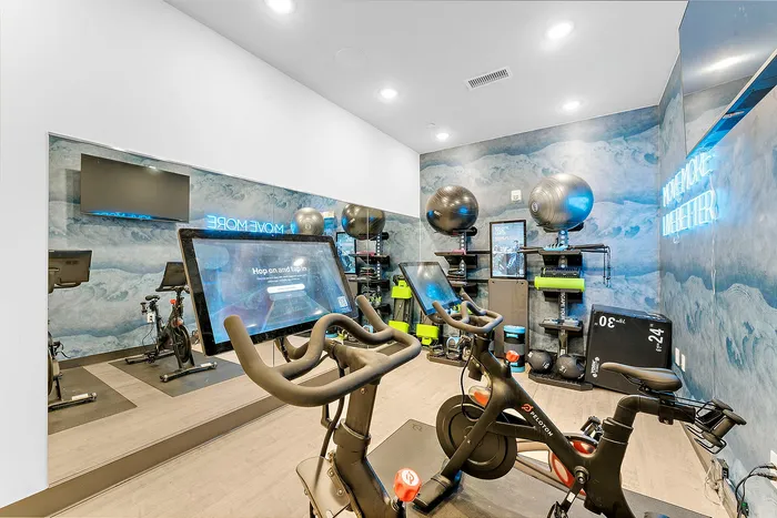 Modern home gym with Peloton bikes and vibrant decor, featuring motivational neon sign and diverse workout equipment.