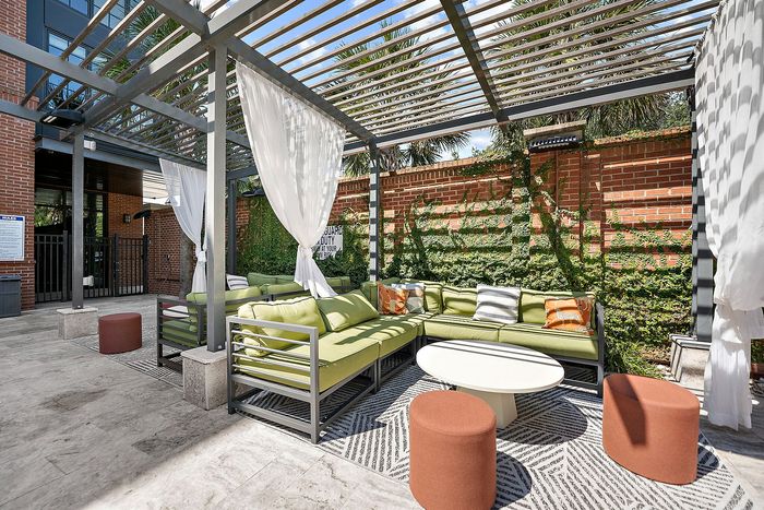 Chic outdoor lounge with modern pergola, cozy green seating, and vibrant accent pillows, perfect for relaxation.