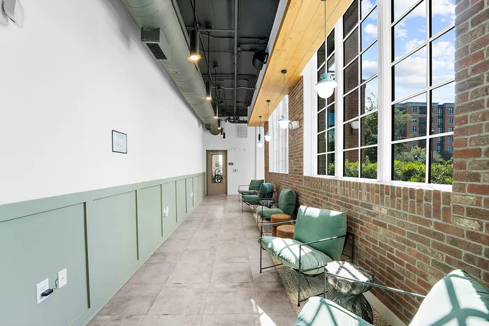 Bright and inviting corridor with modern green seating, large windows, and a chic industrial ceiling, offering a perfect blend of comfort and style.
