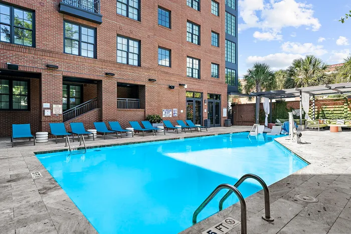 Inviting outdoor swimming pool with stylish blue loungers and vibrant brick architecture, perfect for relaxation and leisure.