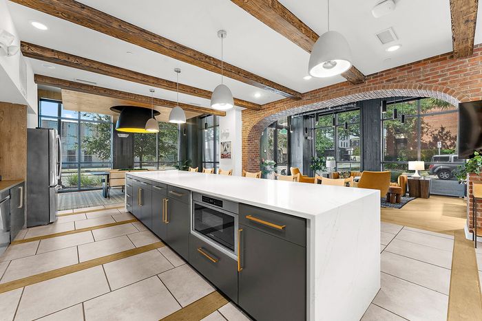 Chic modern kitchen with exposed wooden beams, sleek appliances, and a spacious island, seamlessly flowing into a stylish living area with natural light and urban views.