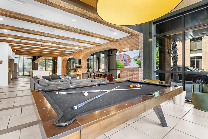 Chic communal space featuring a modern pool table, cozy seating area, exposed brick accents, and expansive windows for natural light.