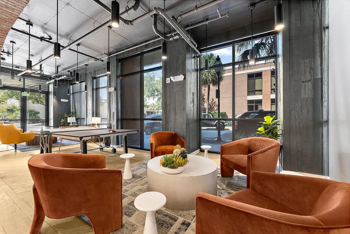 Modern lounge area with plush orange chairs, sleek ping pong table, and large windows offering vibrant views.