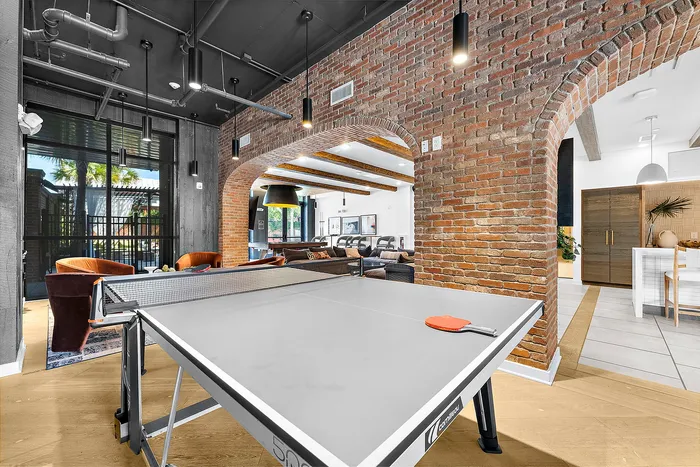 Stunning open-concept space with industrial-chic design featuring a ping pong table, exposed brick walls, and cozy lounge area.