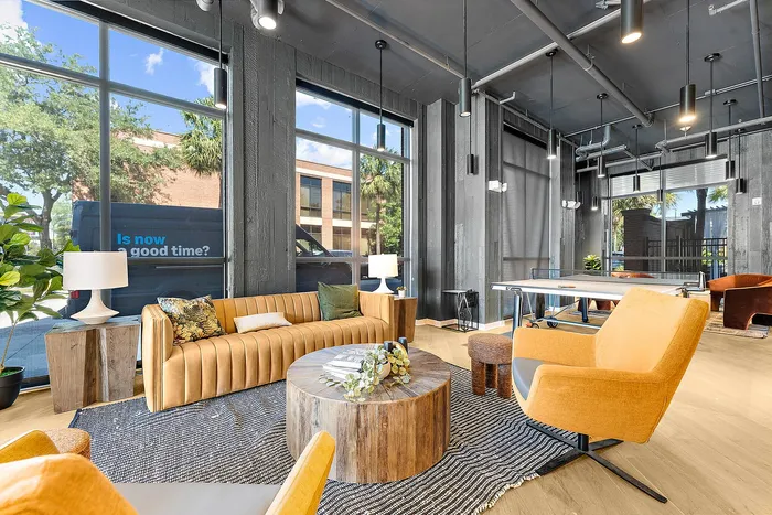 Inviting modern lounge with large windows, vibrant mustard sofas, and a sleek ping pong table, perfect for relaxation and socializing.