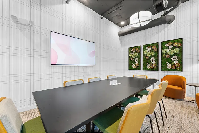 Modern meeting room with a sleek black table, vibrant chairs, and artistic wall d&eacute;cor, perfect for creative collaborations.