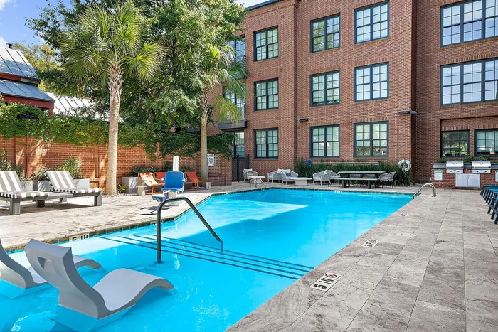 Modern apartment complex with sparkling outdoor pool, stylish lounge chairs, and lush palm trees, offering a serene oasis in a vibrant urban setting.