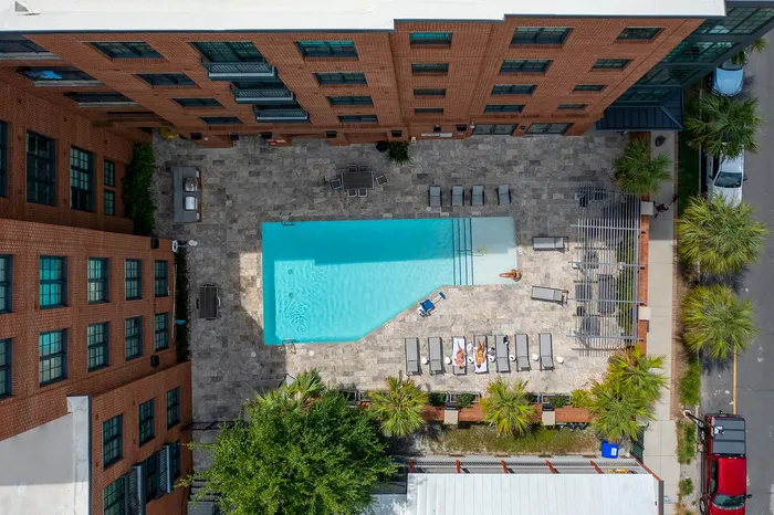 Chic urban apartment complex featuring a luxurious outdoor pool area with sun loungers, surrounded by stylish brick architecture and lush greenery.