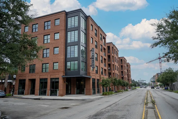 Modern urban apartment building with elegant brick facade, large windows, and lush greenery, under a bright blue sky.