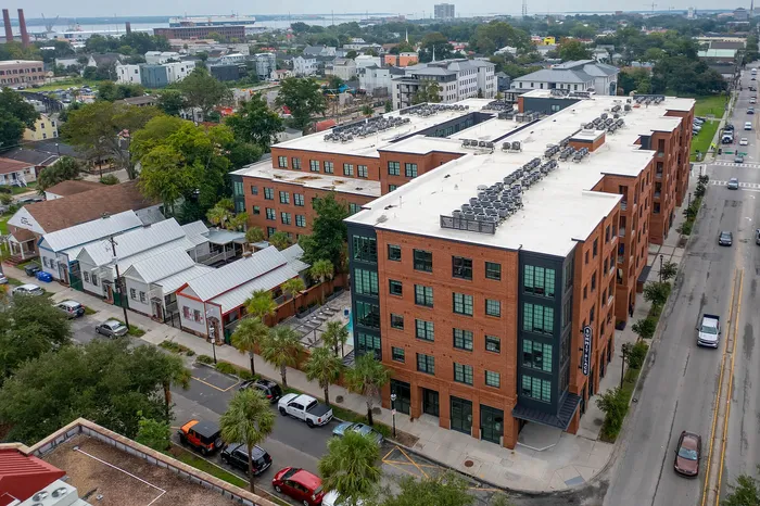 Aerial view of modern red brick apartment complex with lush greenery and lively surrounding neighborhood, highlighting urban living.