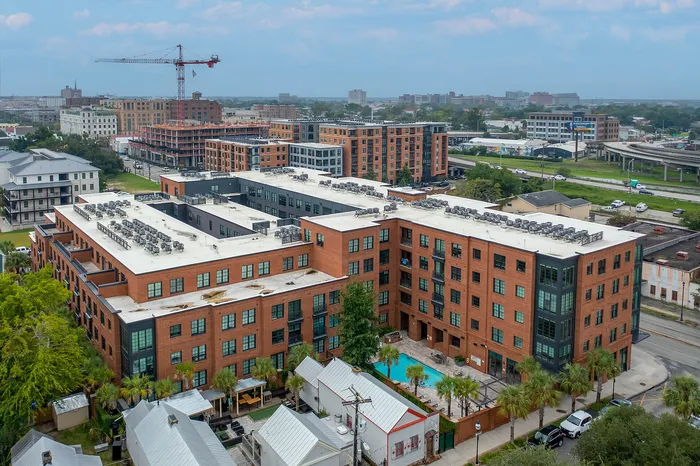 Modern urban apartment complex with brick facade, featuring a refreshing outdoor pool and lush landscaping amidst a vibrant cityscape.