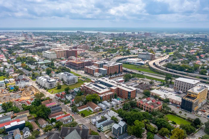 Stunning aerial view of an urban cityscape featuring a vibrant blend of modern architecture and greenery, with easy access to highways and serene water views in the distance.