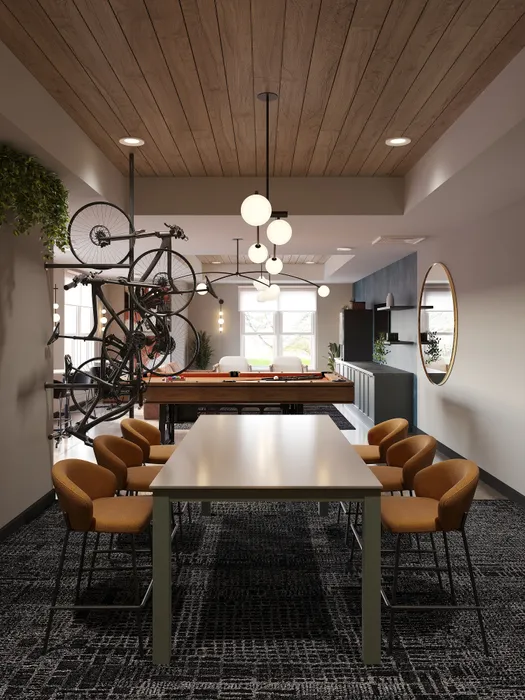 Chic communal space featuring modern dining table, stylish gold chairs, and wall-mounted bike, with billiards table in backdrop under sleek pendant lighting.