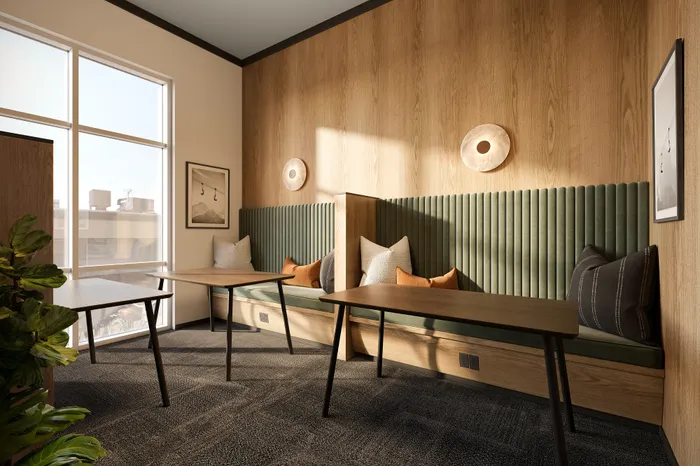 Modern seating nook with plush cushions and wooden tables, featuring stylish wall accents and large sunlit windows.