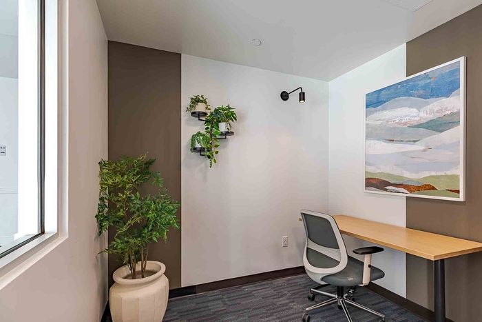 Modern home office nook with stylish white walls, vibrant green plants, and contemporary artwork, offering a serene and productive workspace.