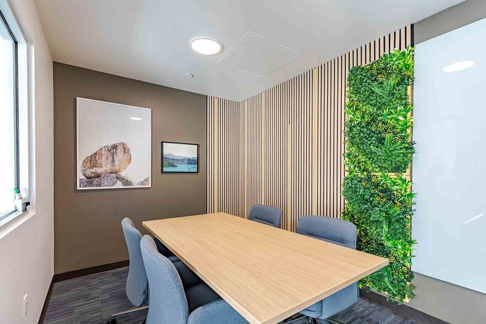 Modern meeting room with stylish wooden accents, natural light, green wall decor, and comfortable seating around a sleek table.