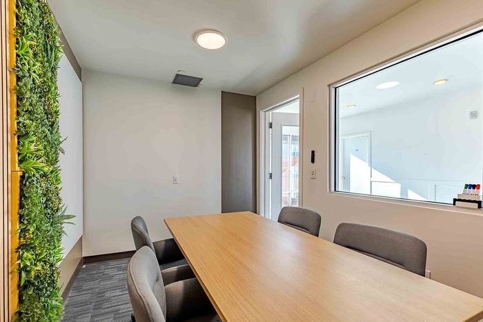 Modern meeting room with a natural green wall, sleek wooden table, and bright lighting.