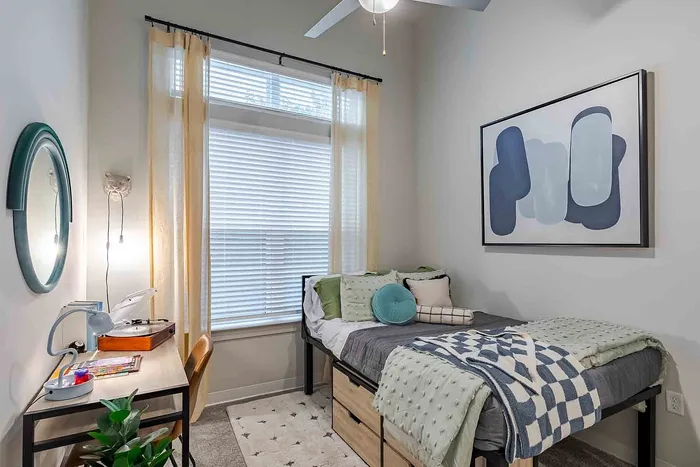 Cozy bedroom featuring a stylish bed with textured blankets, a desk with a trendy lamp and decor, and modern abstract wall art, ideal for students or young professionals.
