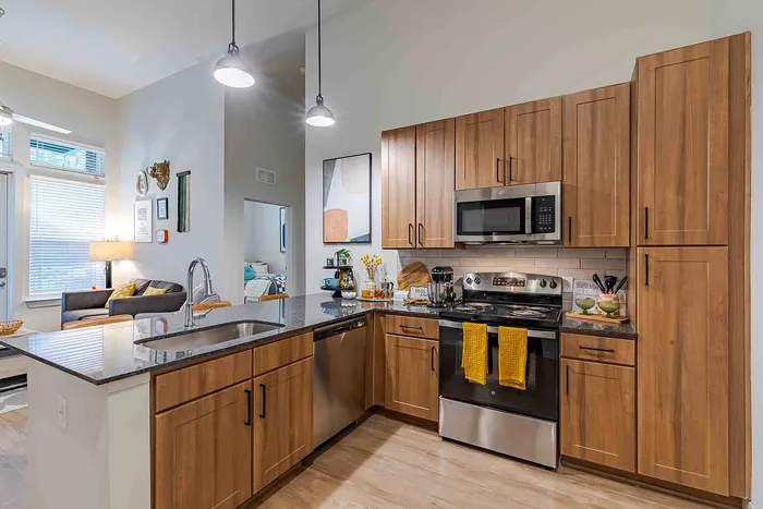 Modern kitchen with sleek wooden cabinets and stainless steel appliances next to a cozy living area with bright windows and stylish decor.