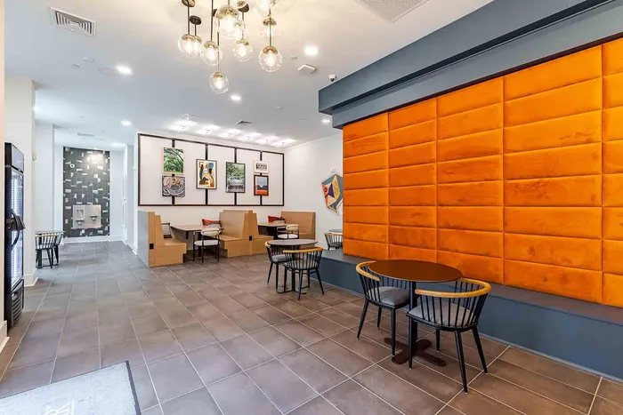 Modern lounge area with striking orange accent wall, elegant lighting fixtures, and stylish art decor.