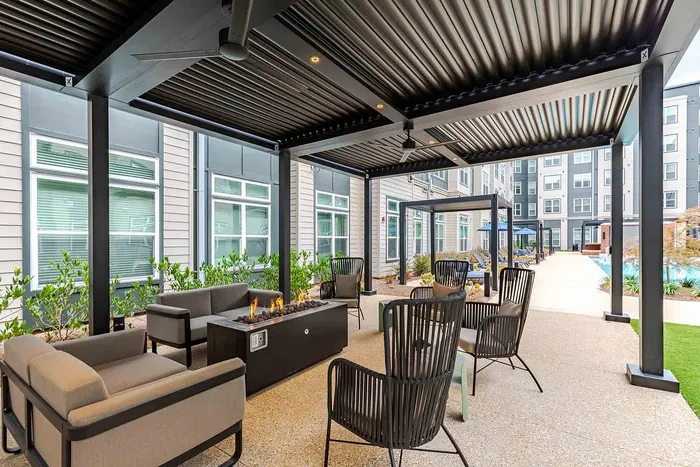 Luxurious outdoor patio area with modern seating and a sleek fire pit, nestled beneath a stylish pergola in a vibrant community courtyard.