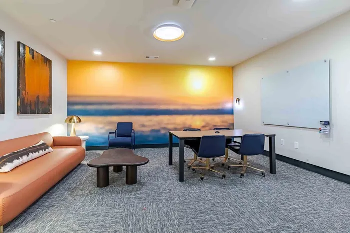 Chic apartment lounge showcasing modern decor with a cozy sofa, sleek conference table, ambient lighting, and a vibrant sunset mural.
