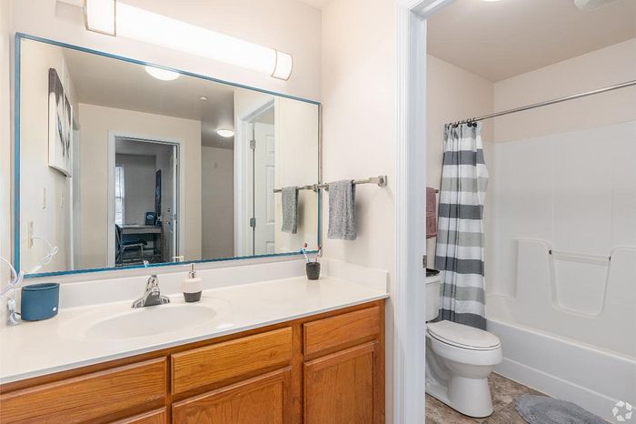 Modern bathroom featuring a sleek single vanity with ample lighting, stylish mirror, and a tub with a striped shower curtain, offering both functionality and elegance.