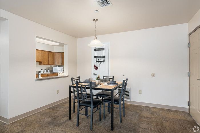 Inviting dining area with a modern table set, adjacent to a warm, open-plan kitchen featuring wooden cabinetry.