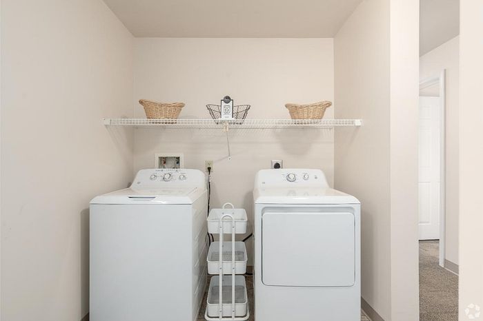 Modern laundry room with sleek white washer and dryer, topped with stylish woven baskets on a convenient overhead shelf.