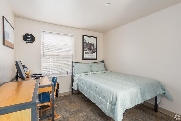 Cozy bedroom with modern decor, featuring a comfortable bed, a study desk by the window, and a stylish wall poster, perfect for a serene living space.