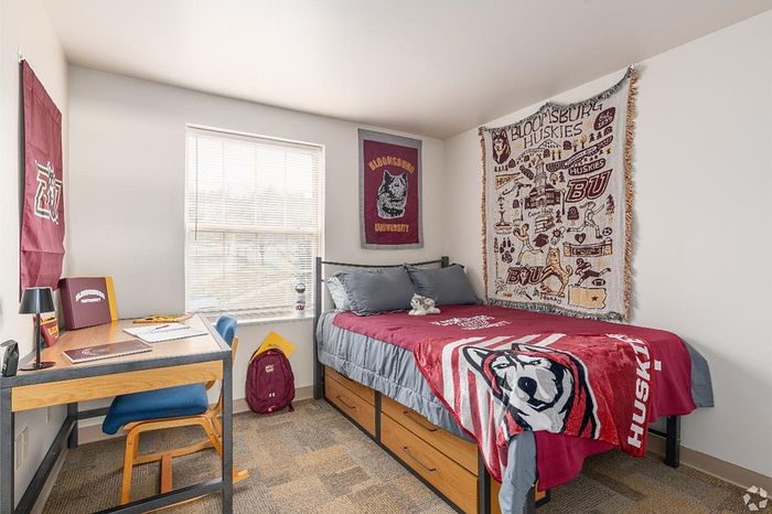Bright and welcoming student dorm room featuring a cozy bed with stylish university-themed decor, a functional study desk, and ample storage space.