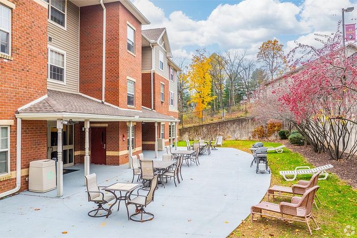 Inviting patio area at a brick apartment building, featuring outdoor seating, grills, and vibrant autumn foliage.