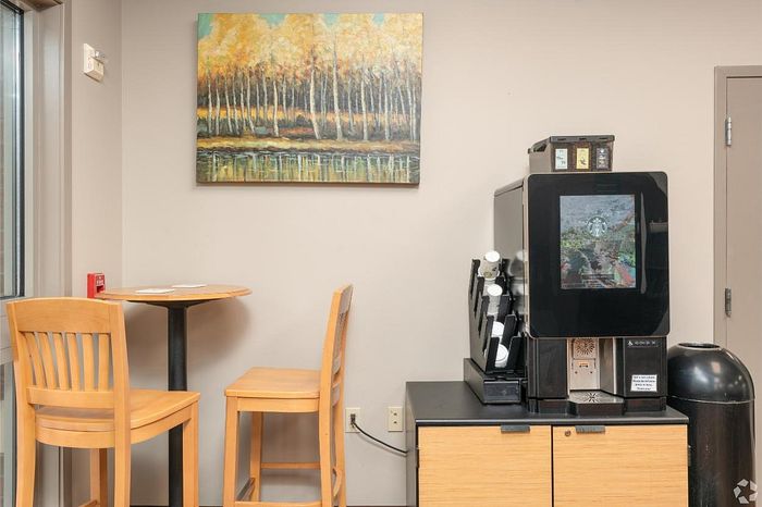Inviting coffee corner with a sleek coffee machine, wooden chairs, a cozy table, and vibrant nature artwork adorning the wall.